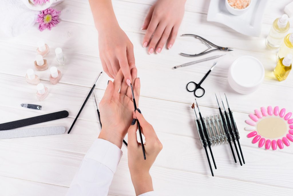cropped image of beautician doing manicure to woman at table with nail polishes, nail files, nail